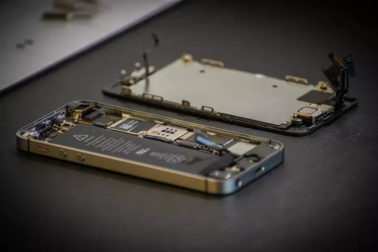 La imagen muestra un teléfono móvil desensamblado, con su carcasa y componentes internos expuestos sobre una superficie. Esta escena resalta la importancia de la "longevidad" en los dispositivos electrónicos, promoviendo la reparación y mantenimiento como parte esencial de su ciclo de vida. Al permitir el acceso y la sustitución de piezas, se extiende la vida útil del producto, contribuyendo a una economía más sostenible y reduciendo el impacto ambiental asociado con la producción de nuevos dispositivos.